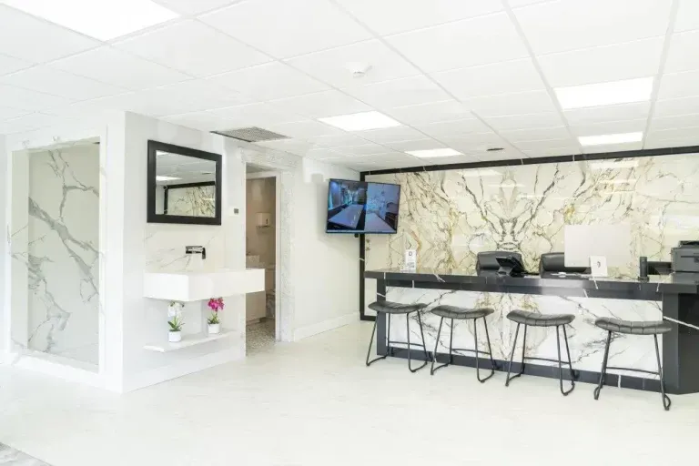 Bright white office lobby with reception desk, TV, marble wall, and shelving unit