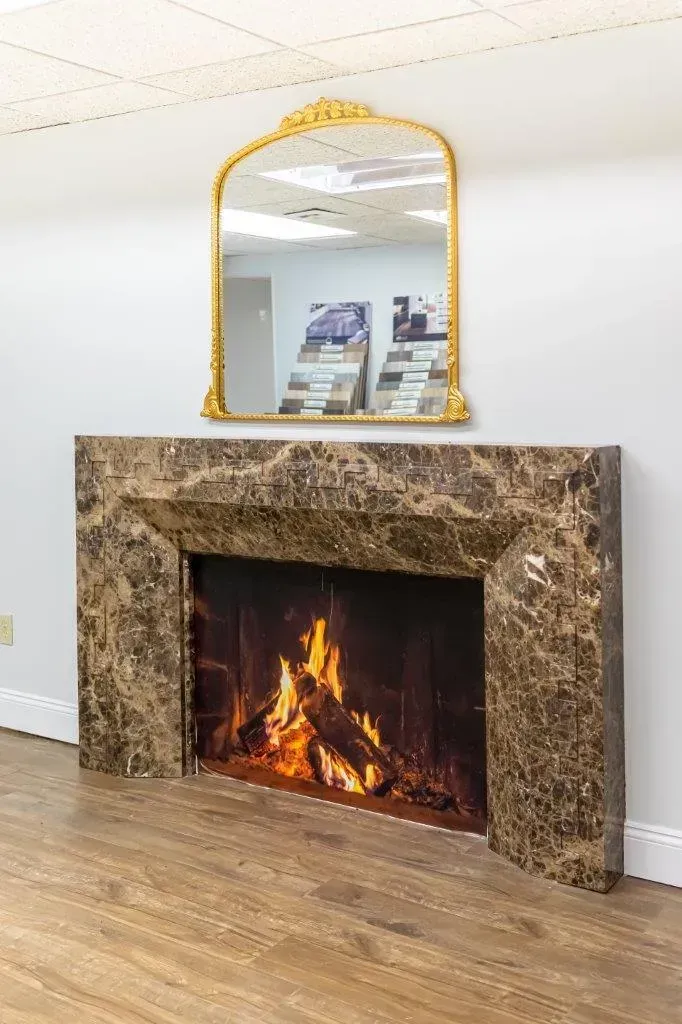 Empty room with wood floor, stone fireplace, and a gold-framed mirror above it