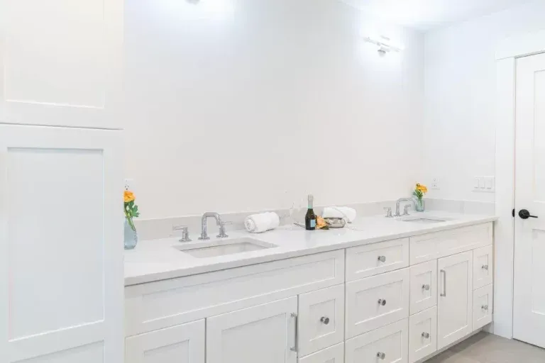 Bright white bathroom vanity with double sinks, mirrors, and small flower vases on the countertop.
