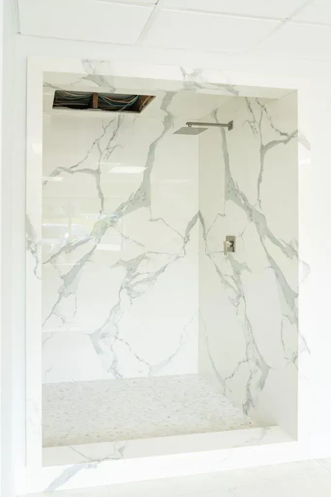 Tiled shower with white marble-look walls, recessed niche, and showerhead opening on the ceiling