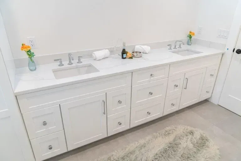 White bathroom vanity with double sinks, countertop accessories, and a small rug on the floor