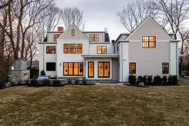 White two-story house with lit windows and a large lawn at dusk