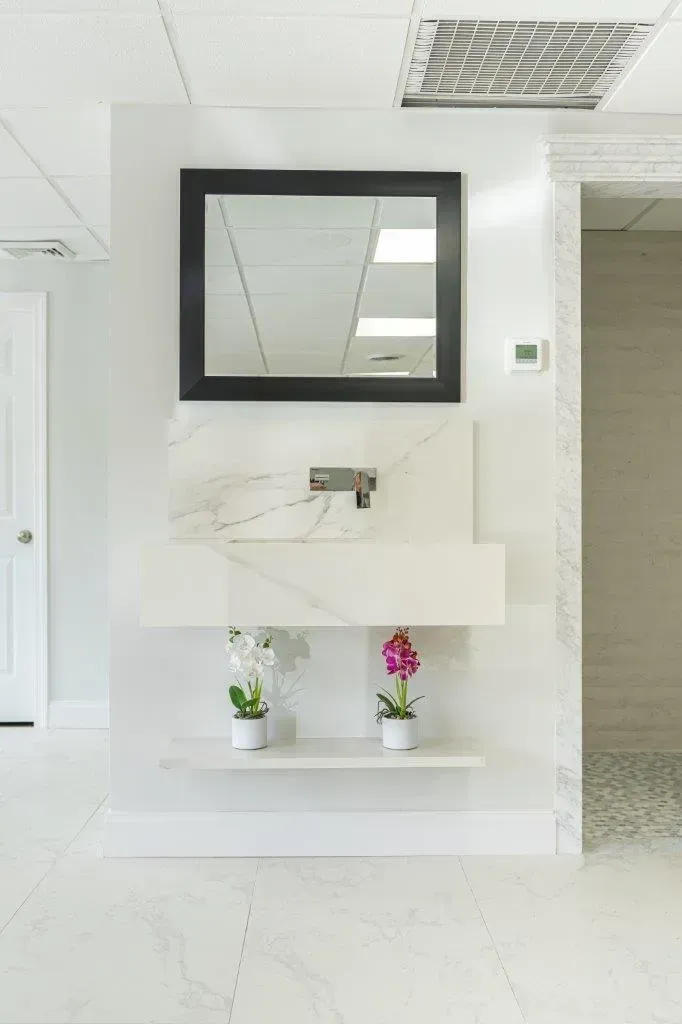 Modern white hallway with wall mirror, sink, and two small potted flowers