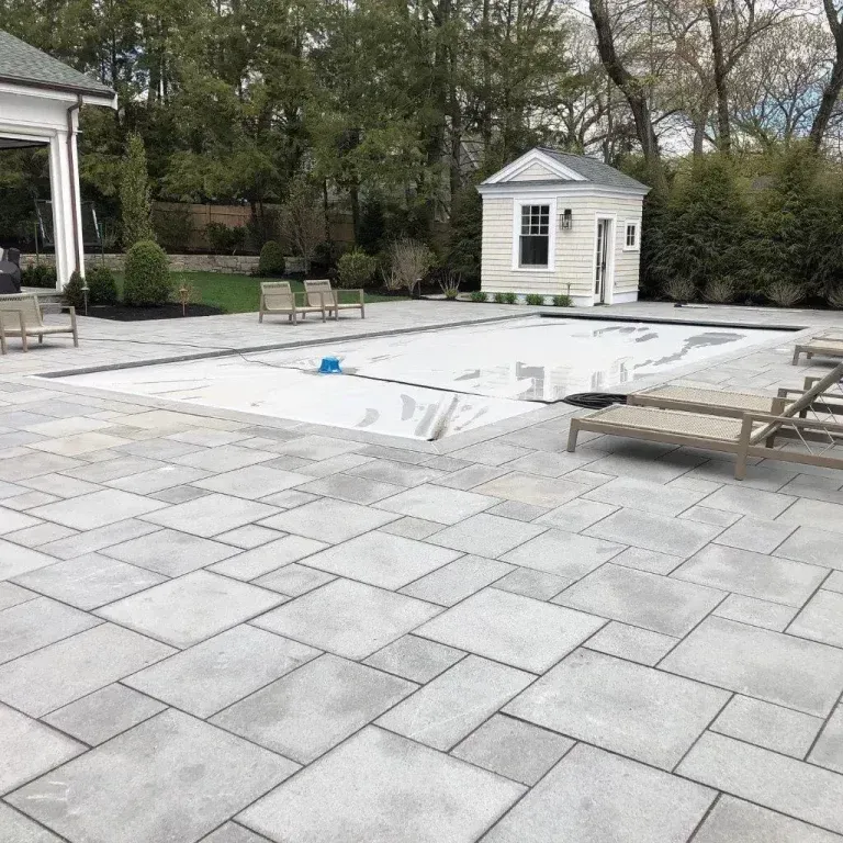 Backyard patio with a covered pool, lounge chairs, and a small white shed near trees