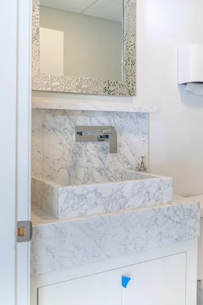 Marble bathroom vanity with square sink, large mirror, and wall-mounted soap dispenser