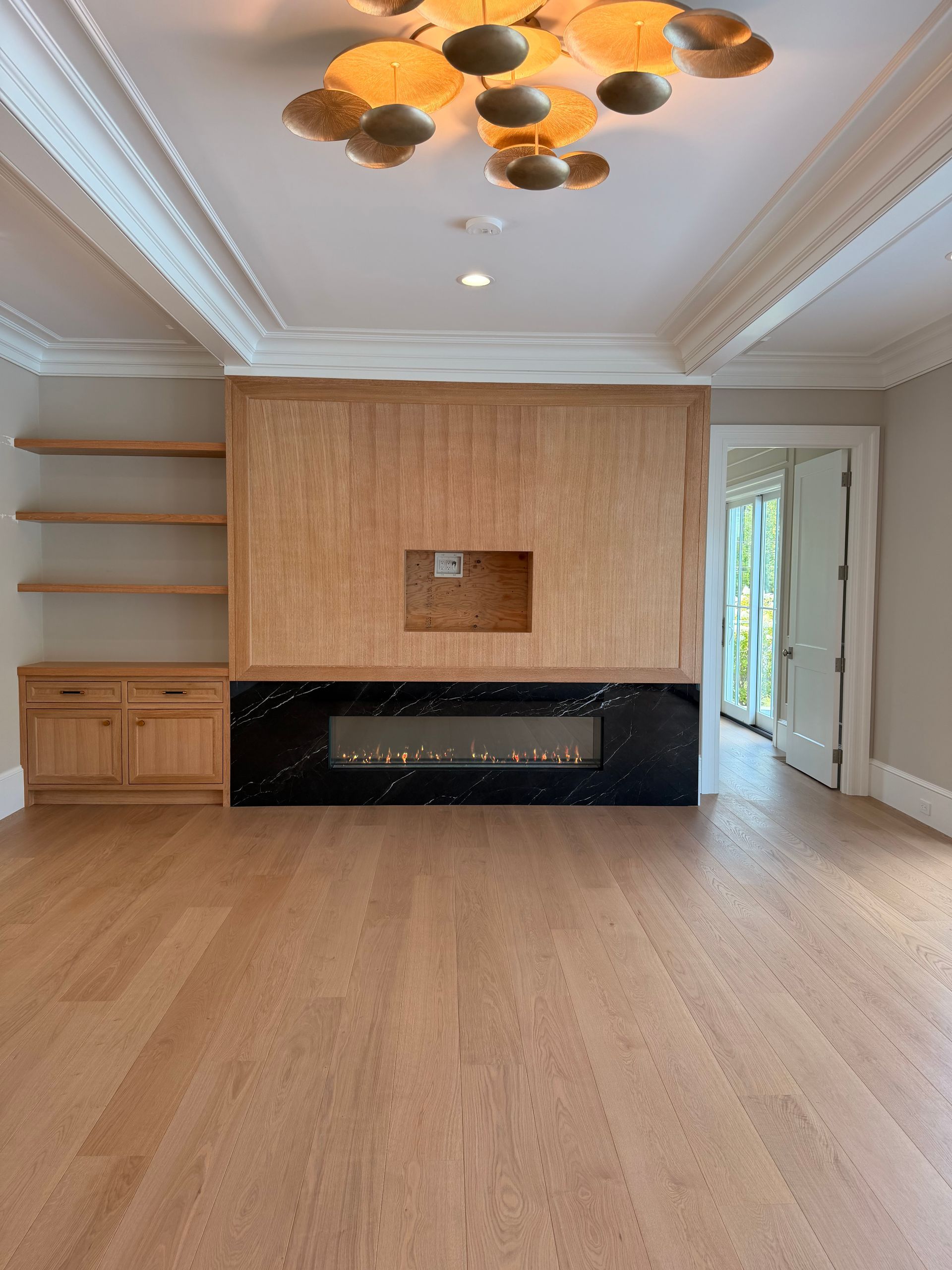 Empty modern living room with light wood floors, built-in shelving, and a black fireplace accent wall