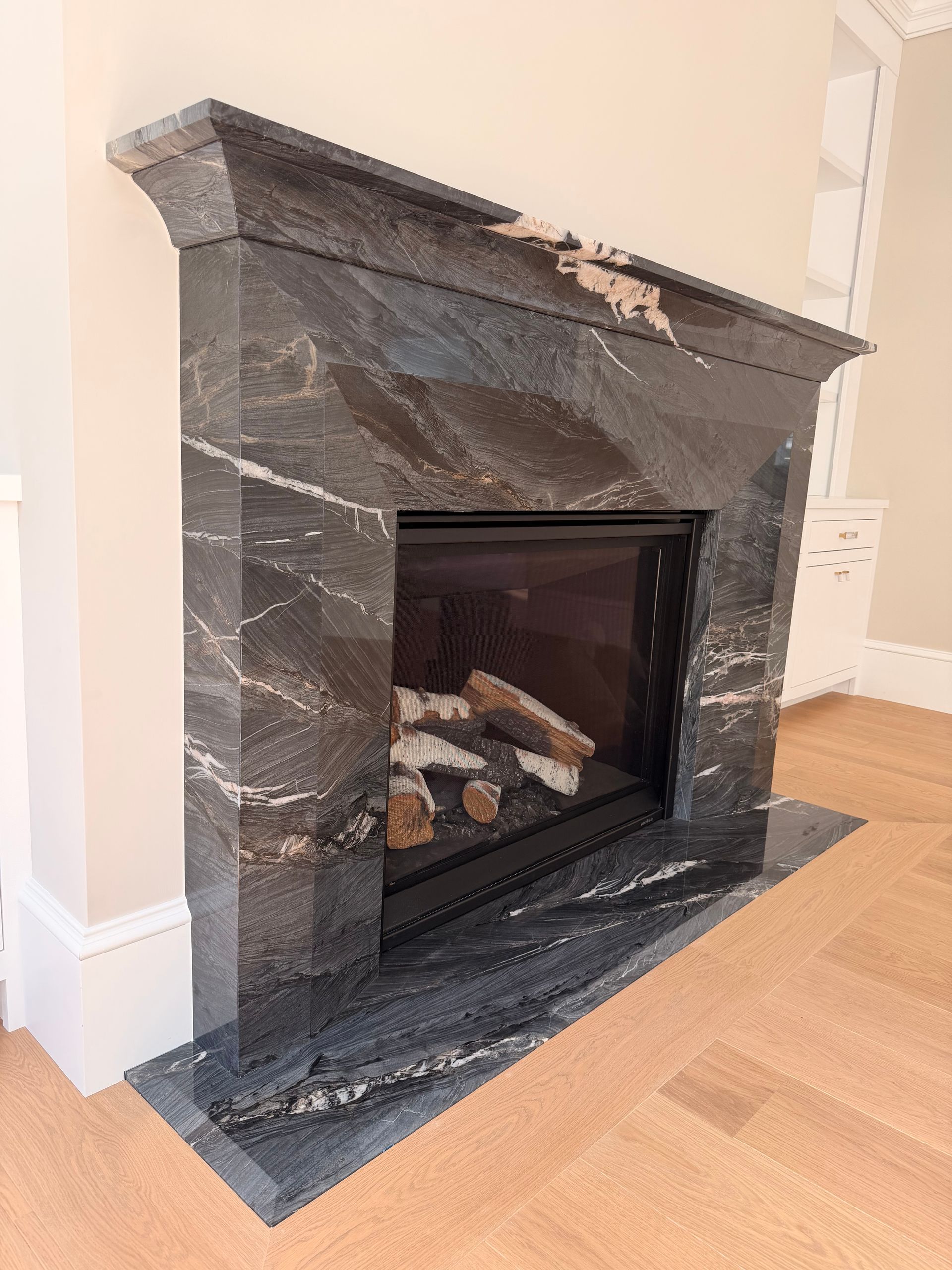 Dark marble fireplace with black firebox in a light room, set on a matching hearth.