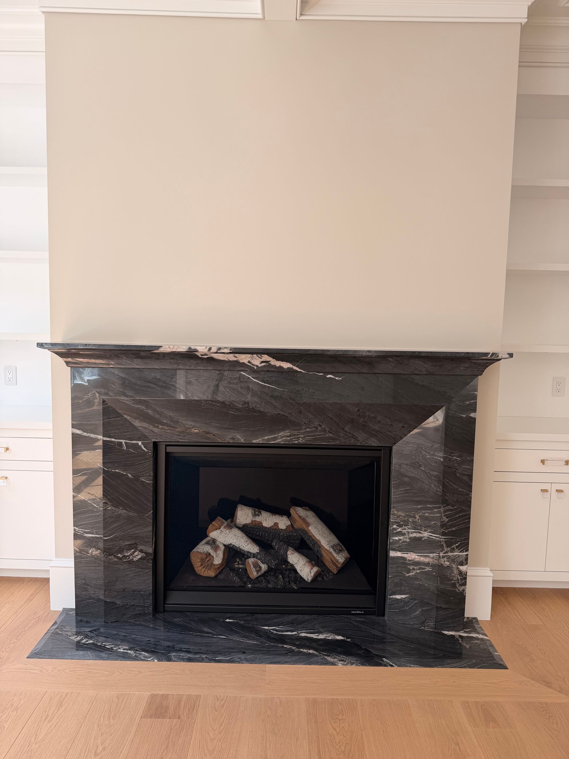 Black marble fireplace with a gas log insert against a beige wall in a living room