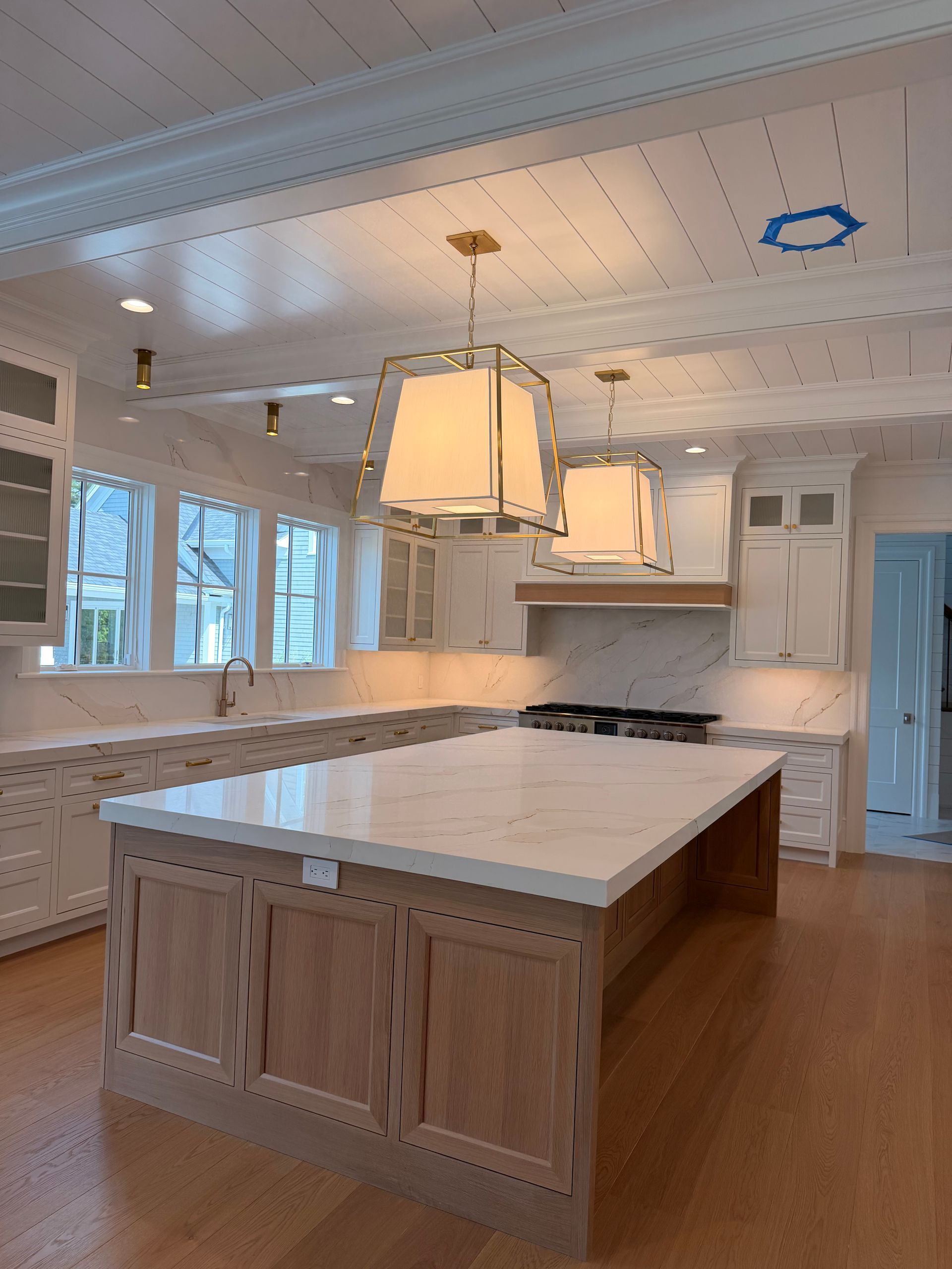 Bright kitchen with large island, white cabinets, hanging pendant lights, and wood floors