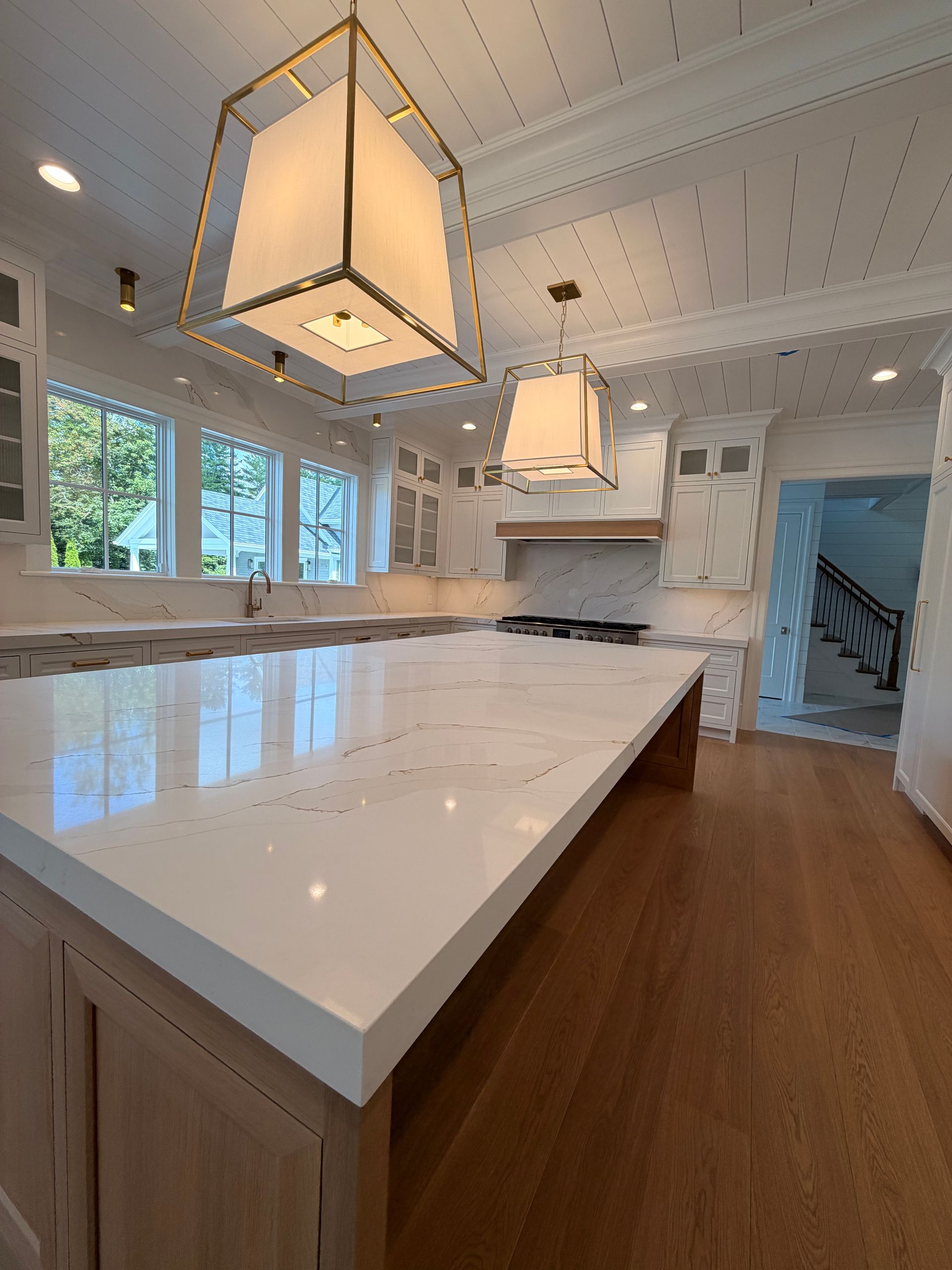 Bright white kitchen with large island, pendant lights, windows, and hardwood floors
