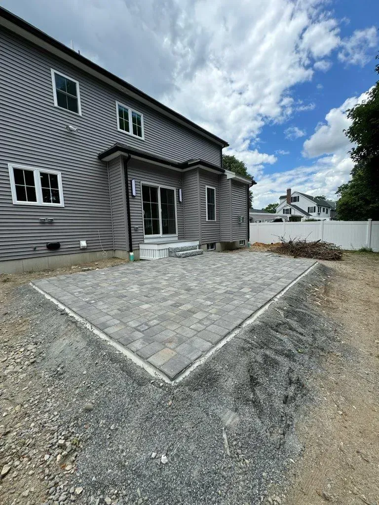 Gray house exterior with stone walkway, gravel yard, and white fence under cloudy sky