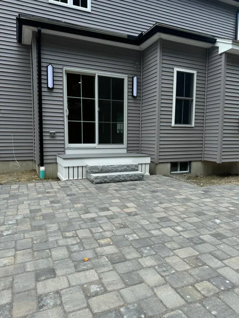Back patio with gray paver stones, steps, and sliding glass door on a gray house