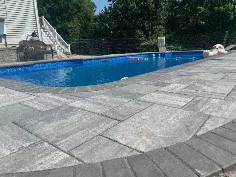 Backyard pool with blue water beside a gray stone patio, stairs, and lounge chairs nearby