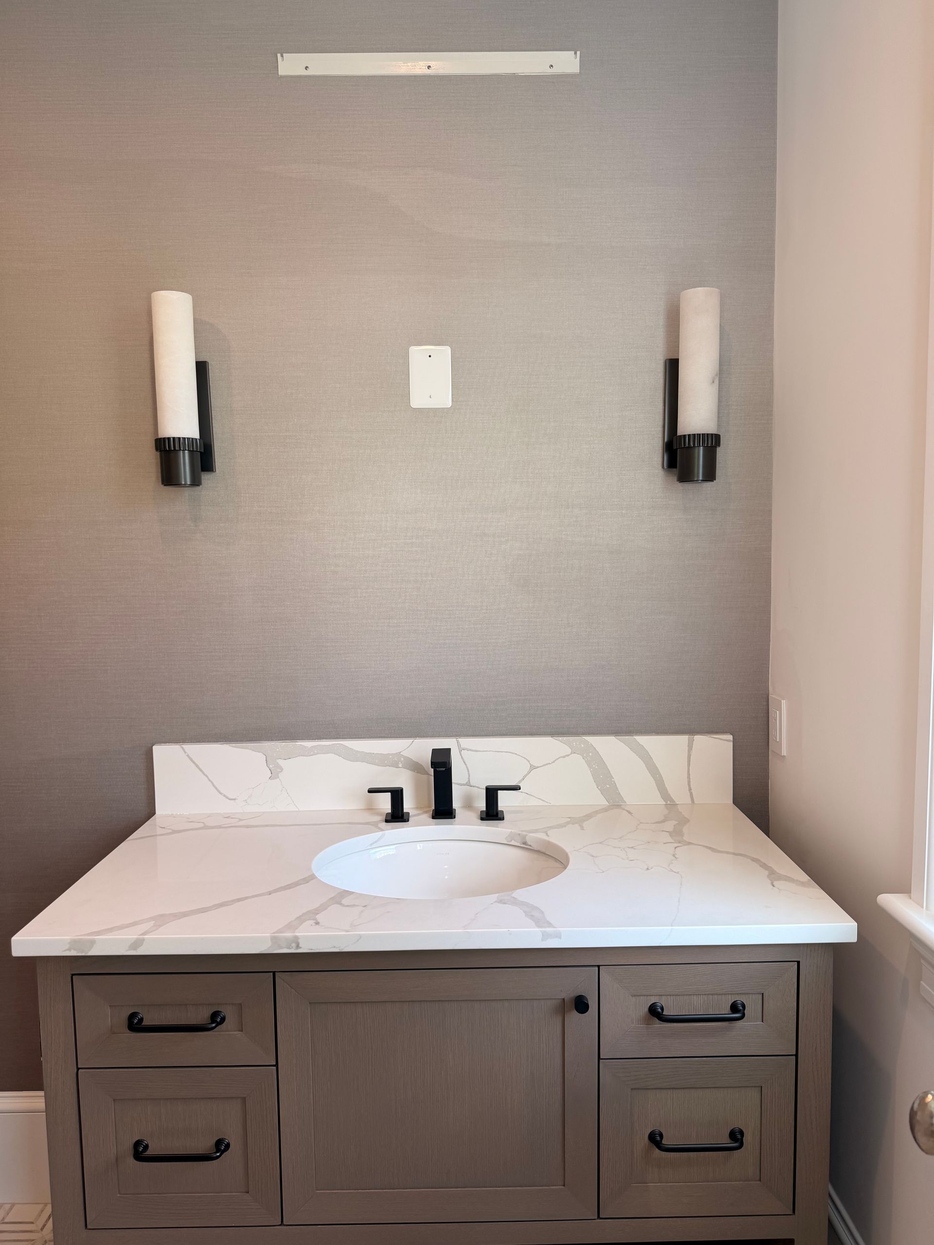 Modern bathroom vanity with white marble countertop, round sink, dark wood cabinets, and wall sconces.