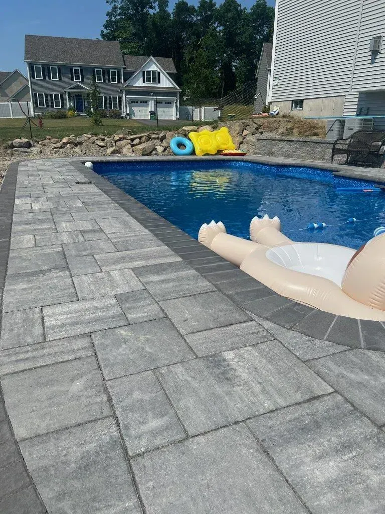 Backyard pool with floating inflatable and gray stone patio beside houses and trees