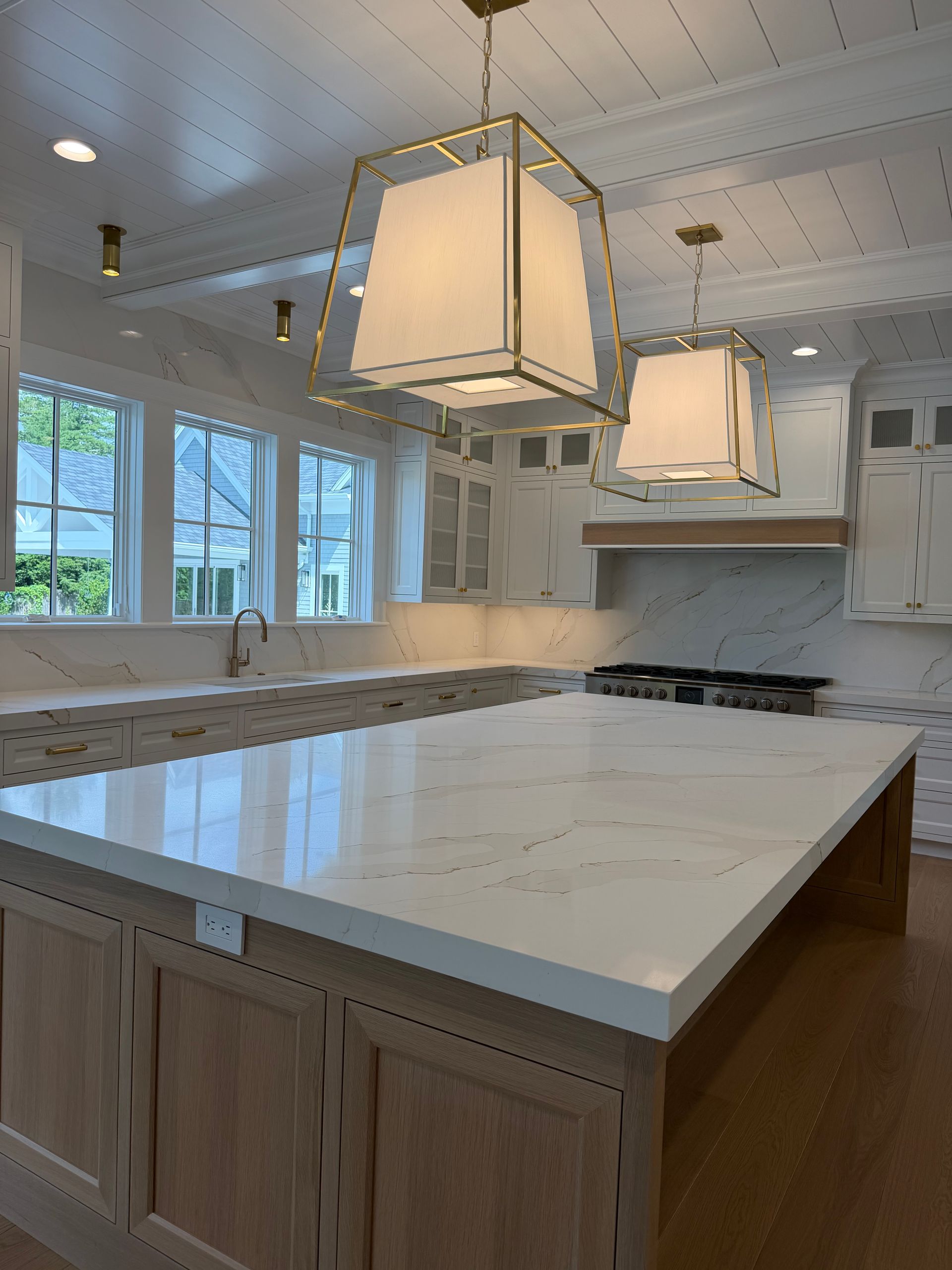Bright modern kitchen with white island, marble countertops, pendant lights, and large windows