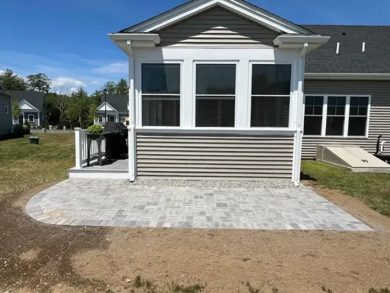 Small white house exterior with a screened porch and stone patio in front