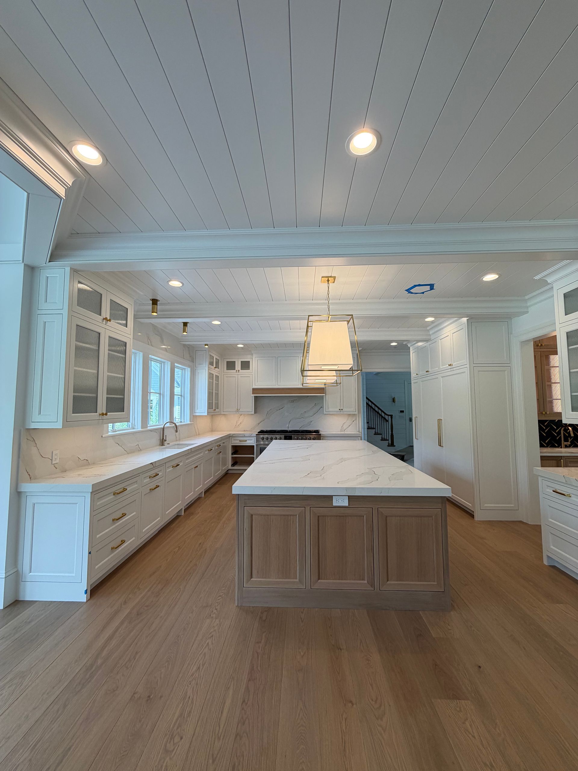 Bright white kitchen with a large island, wood floors, and built-in cabinetry under recessed lights