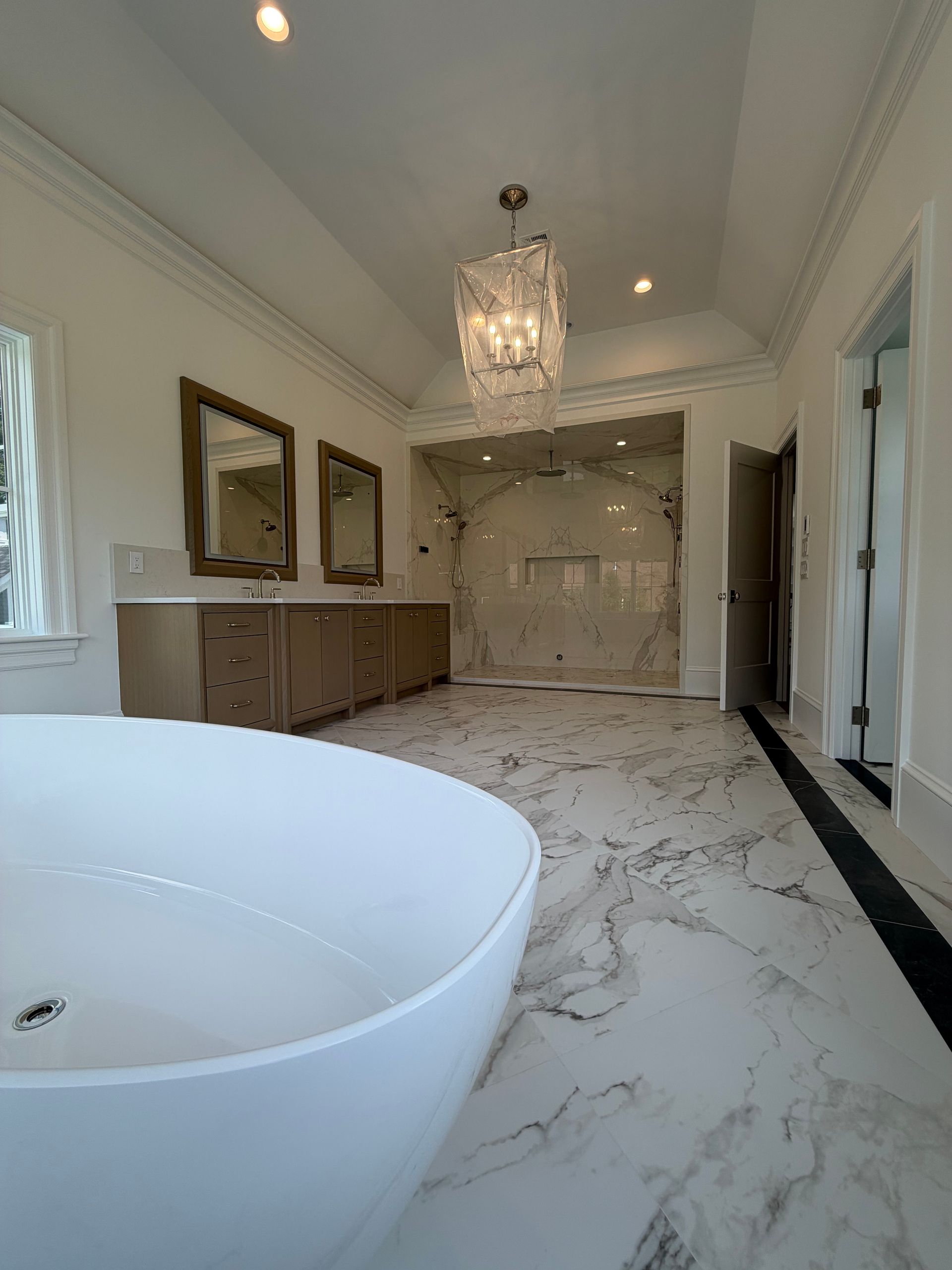 Elegant white marble bathroom with freestanding tub, chandelier, mirrors, and double vanity