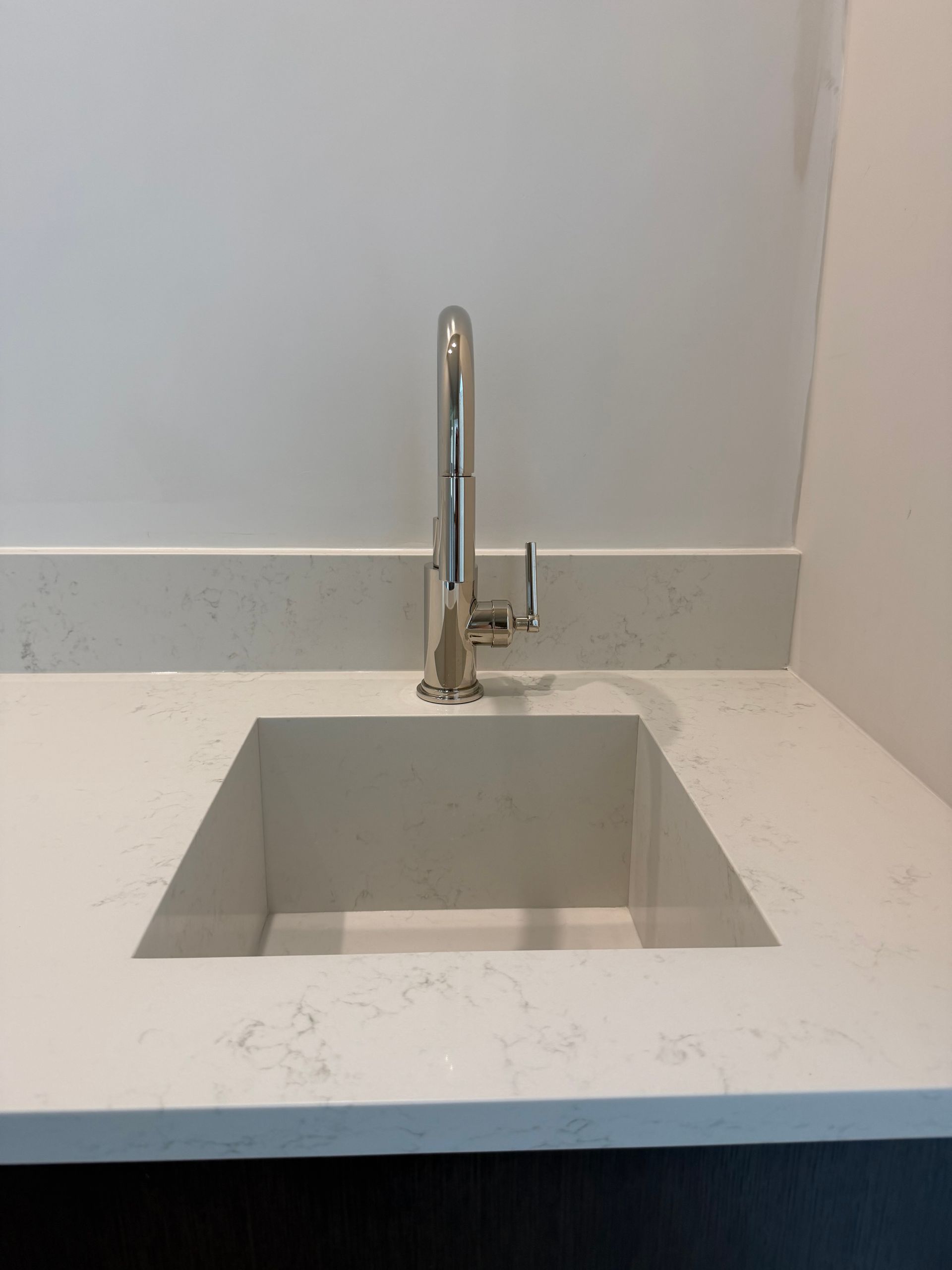 Modern kitchen sink with a chrome faucet and white countertop against a light gray backsplash