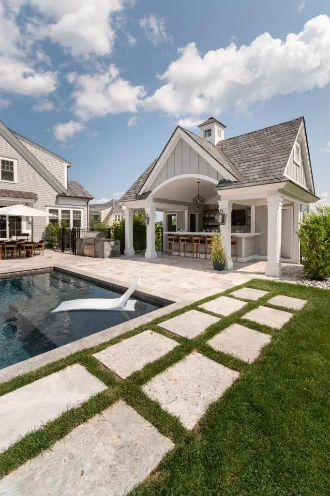Modern backyard with pool, white cabana, and stone path under a bright sky