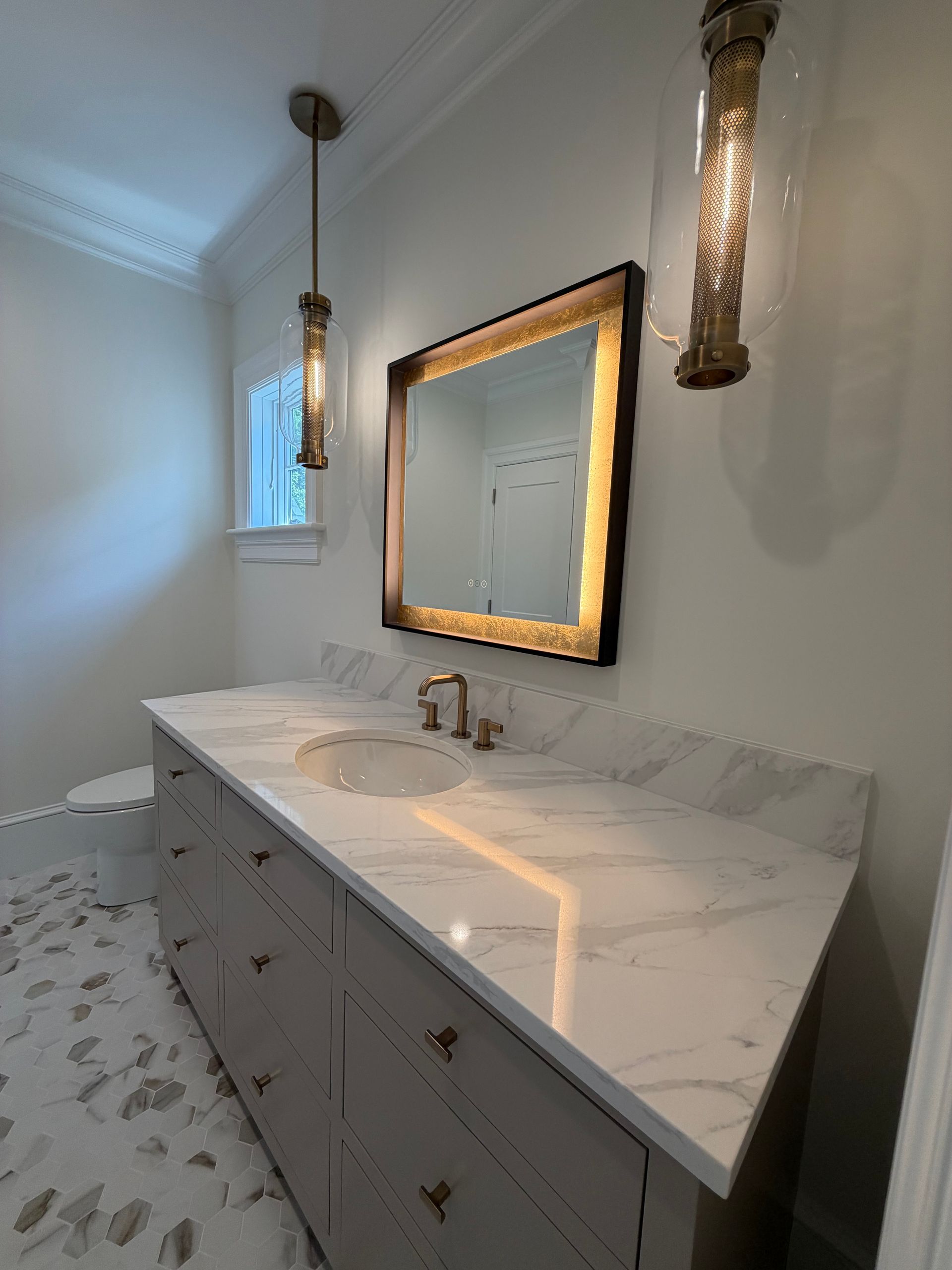 Modern bathroom vanity with white marble countertop, gold-framed mirror, and brass sconces.