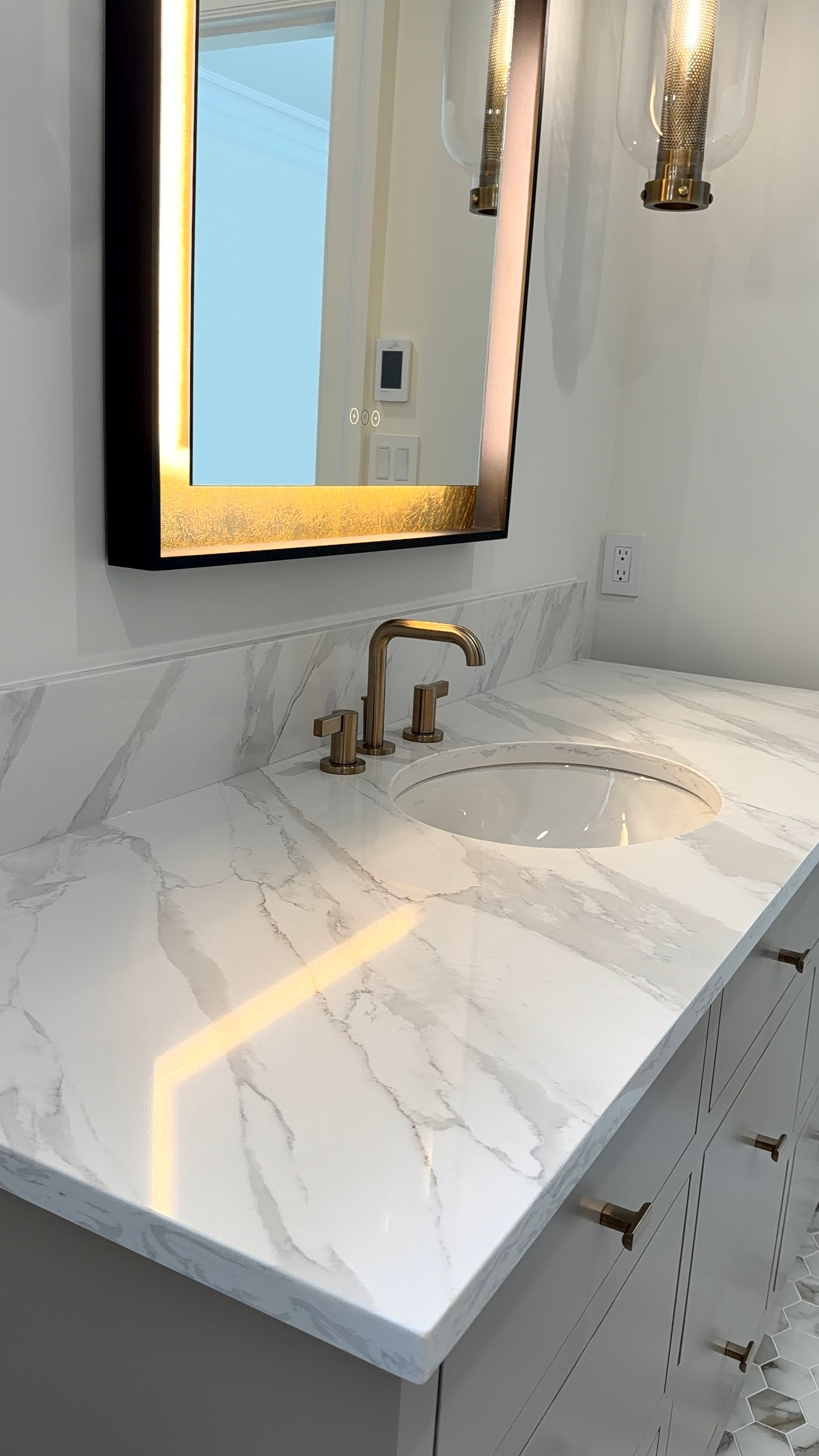 Modern bathroom vanity with white marble countertop, gold faucet, and illuminated mirror