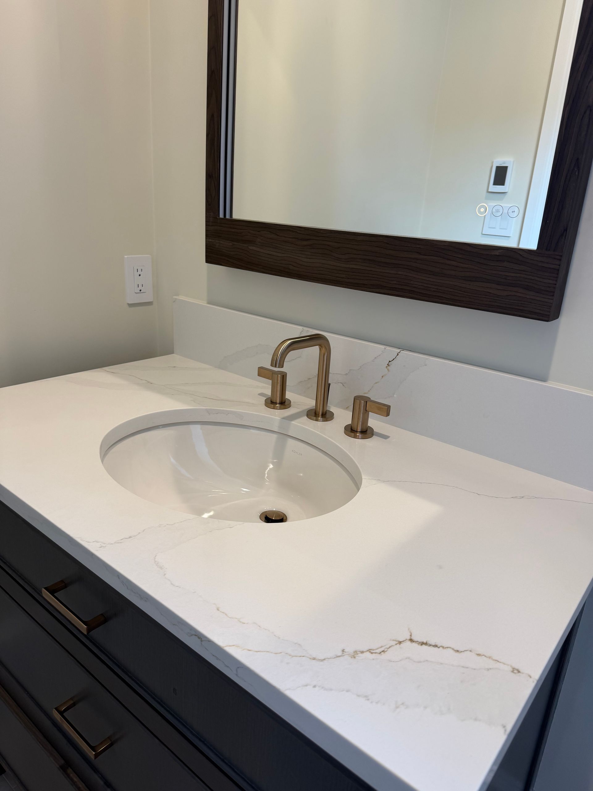 Modern bathroom vanity with white countertop, oval sink, dark wood drawers, and gold faucet under a mirror
