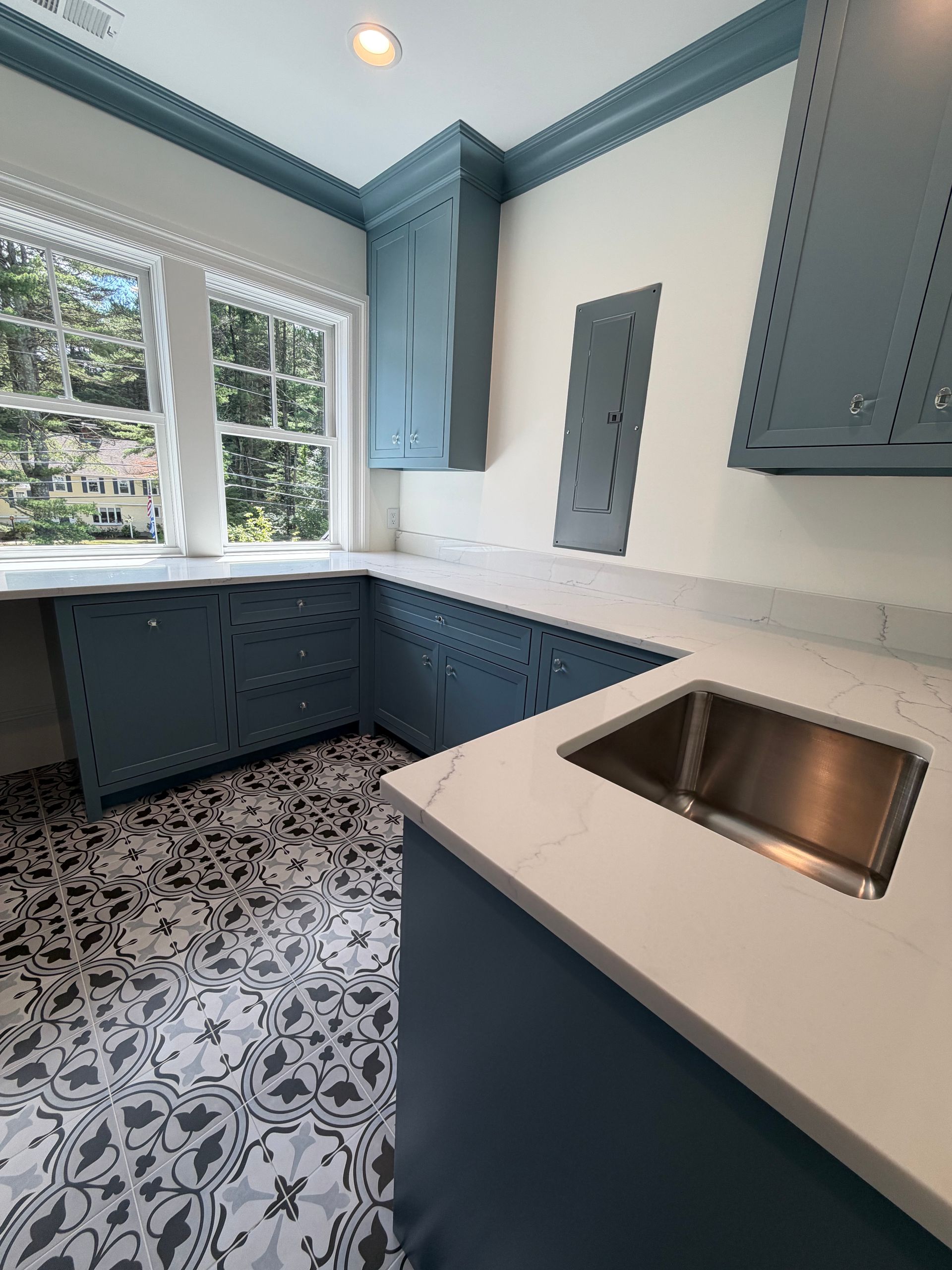 Bright blue and white kitchen with patterned tile floor, large window, and stainless sink