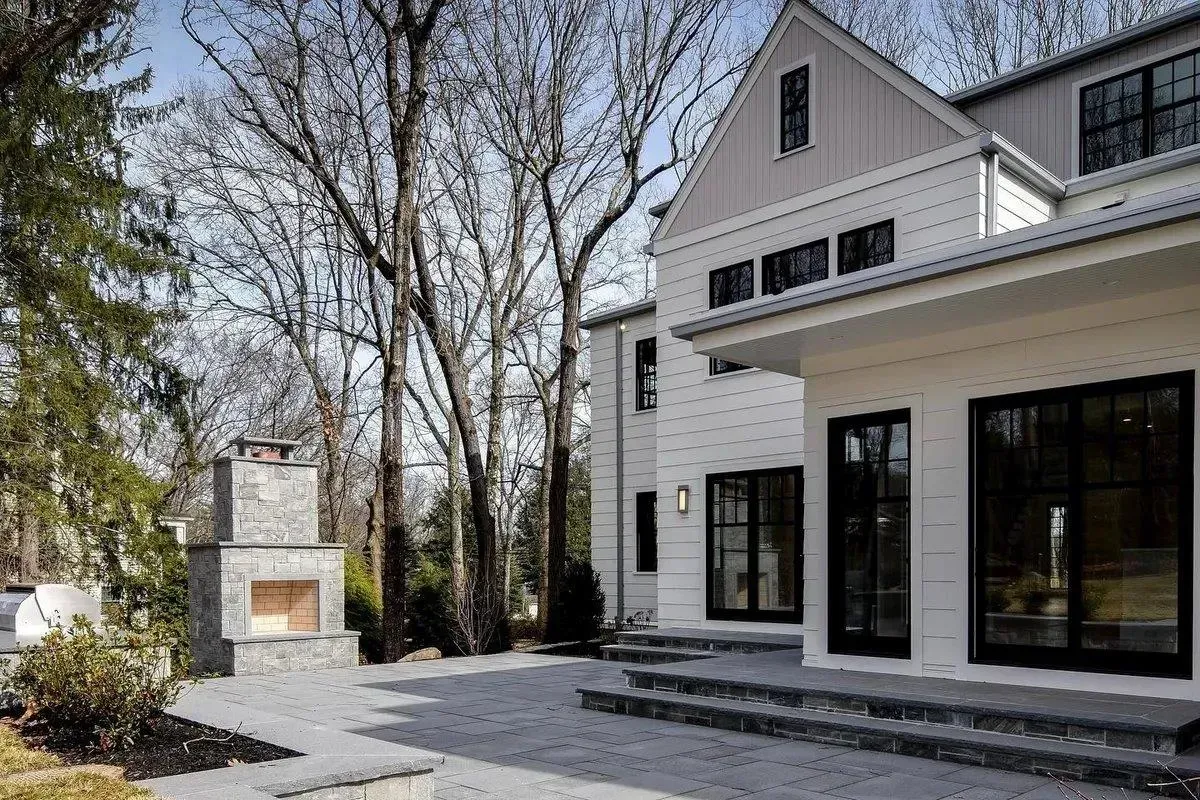 Modern white house with large windows, front steps, and a stone patio beside leafless trees