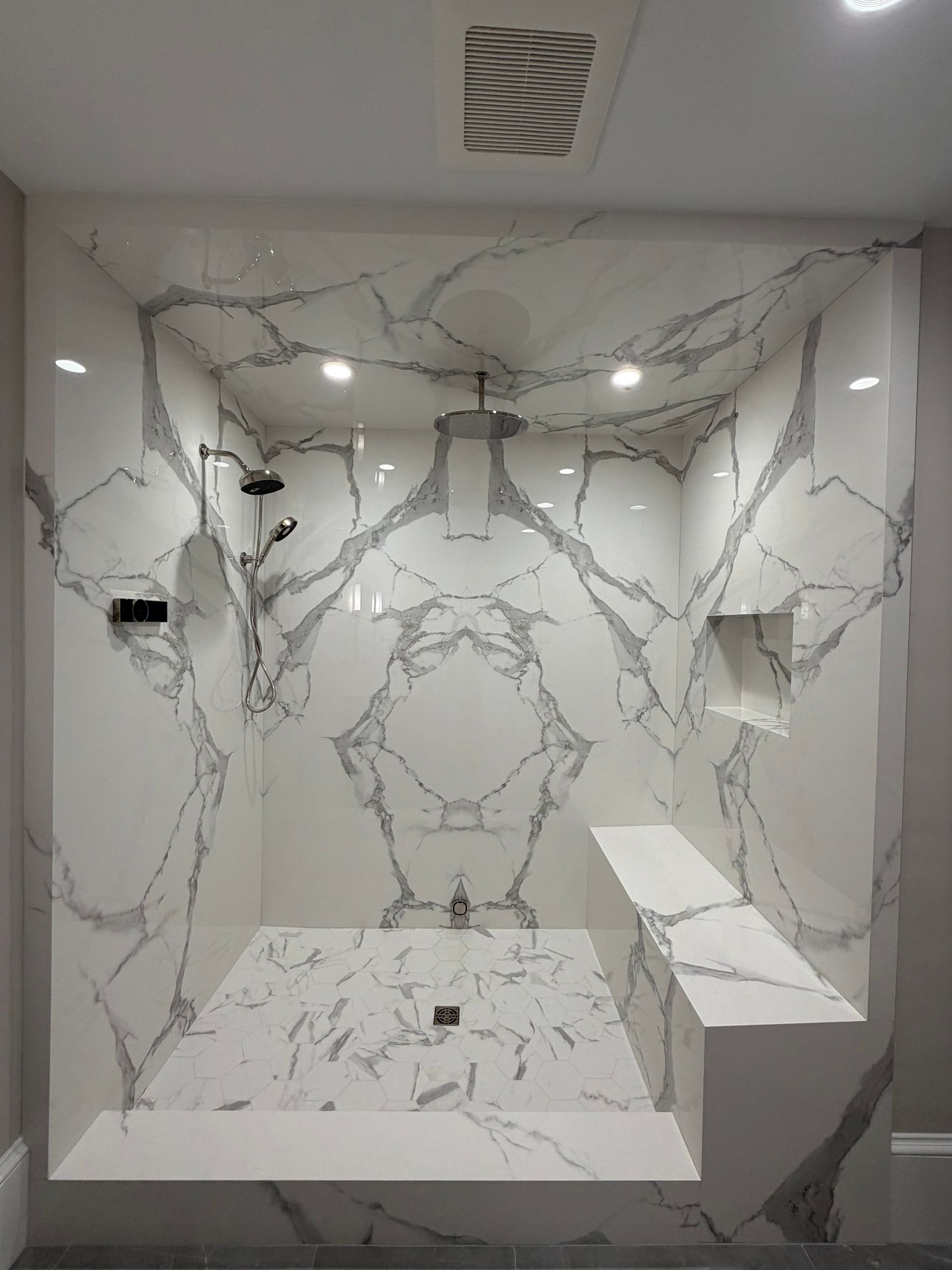 Modern marble-tiled bathroom with a walk-in shower and bench seating.