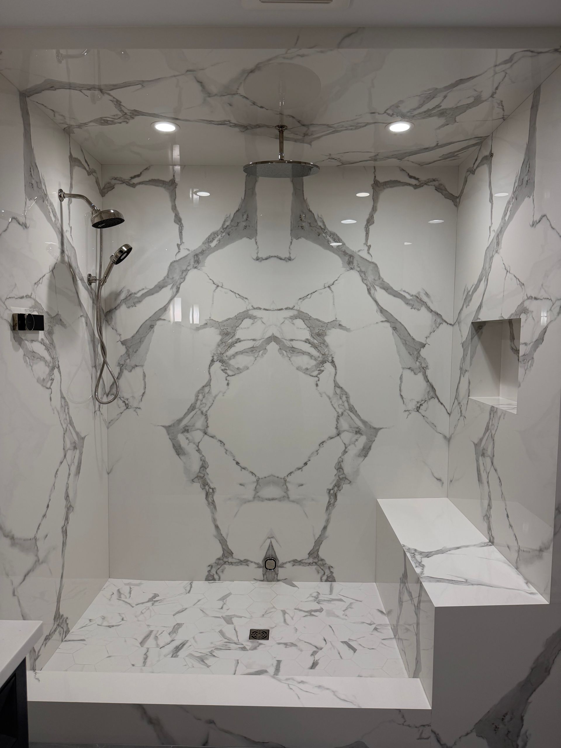 Marble-tiled shower stall with built-in bench, recessed niches, and overhead lights