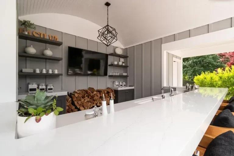 Bright modern kitchen with a white island, gray shelves, TV, and open doors to a green patio.