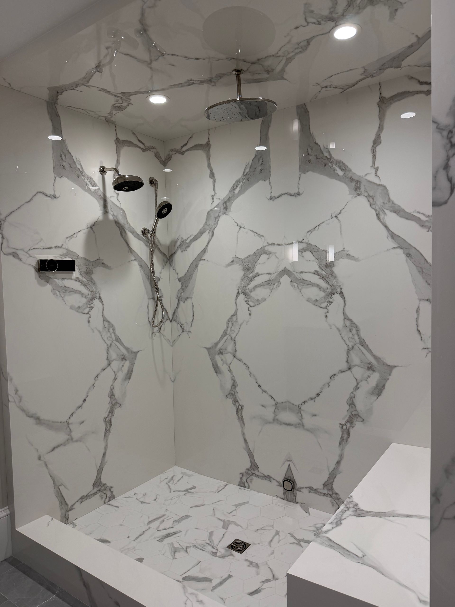 Modern bathroom with marble-look tile walls, rainfall shower, and built-in bench seat.