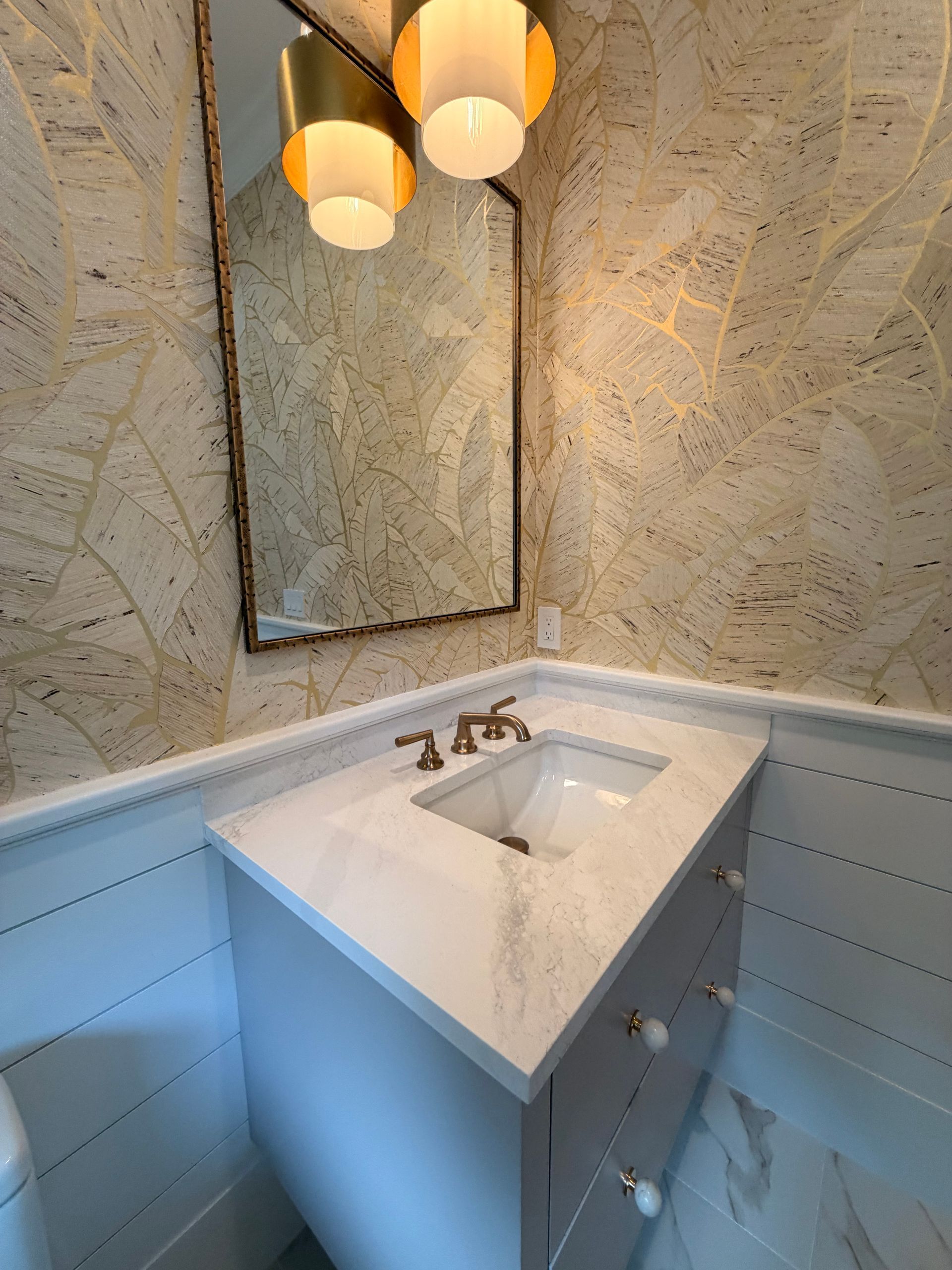 Small bathroom vanity with white sink, mirror, marble-patterned walls, and pendant lights.