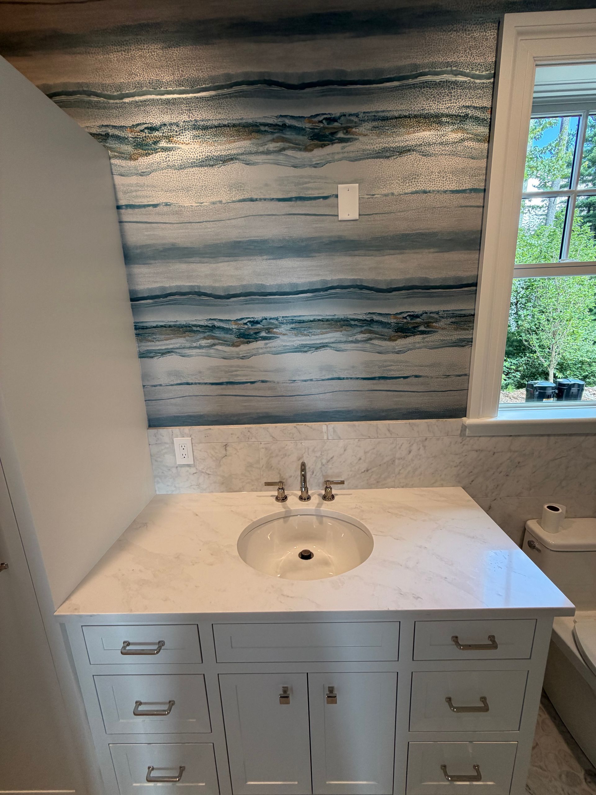 Bathroom vanity with white countertop, gray cabinets, and a round sink beneath a striped wall and window.