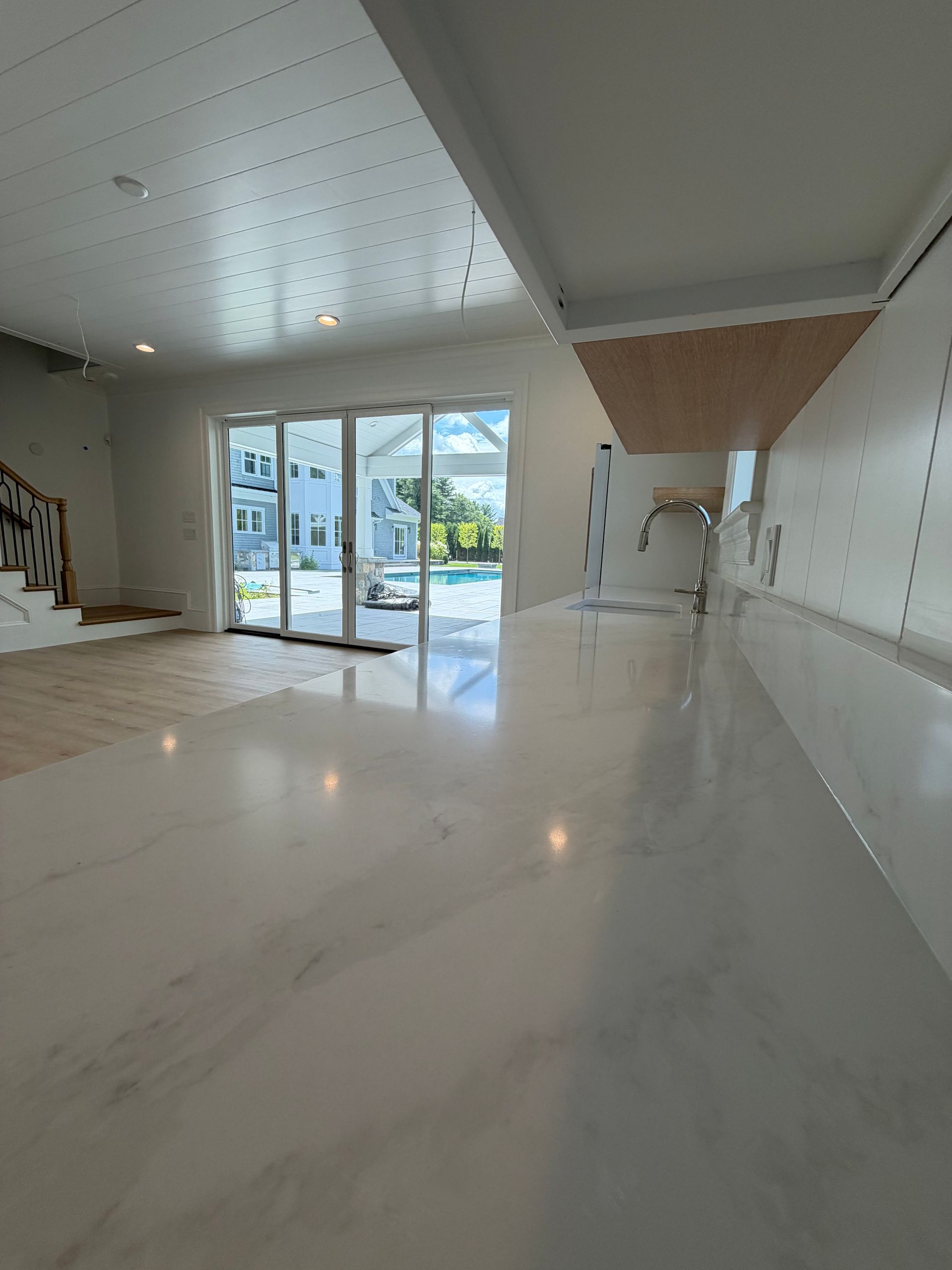 Bright empty modern living room with glossy white floor, staircase, and large glass doors opening to a garden.