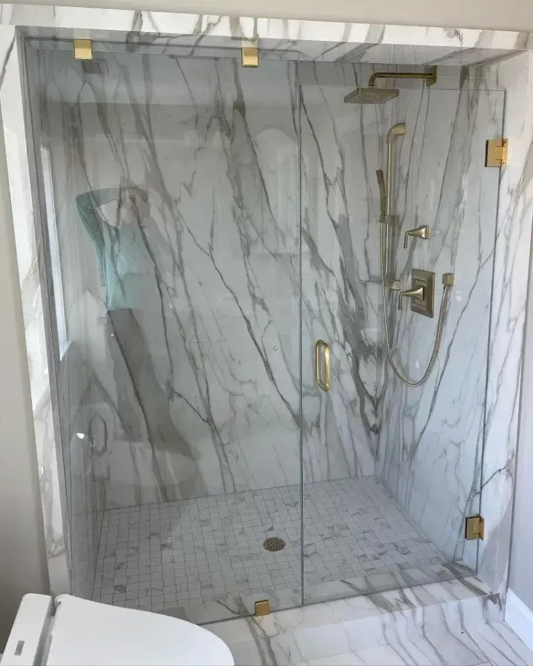 Marble-tiled walk-in shower with glass door, brass fixtures, and bench seat