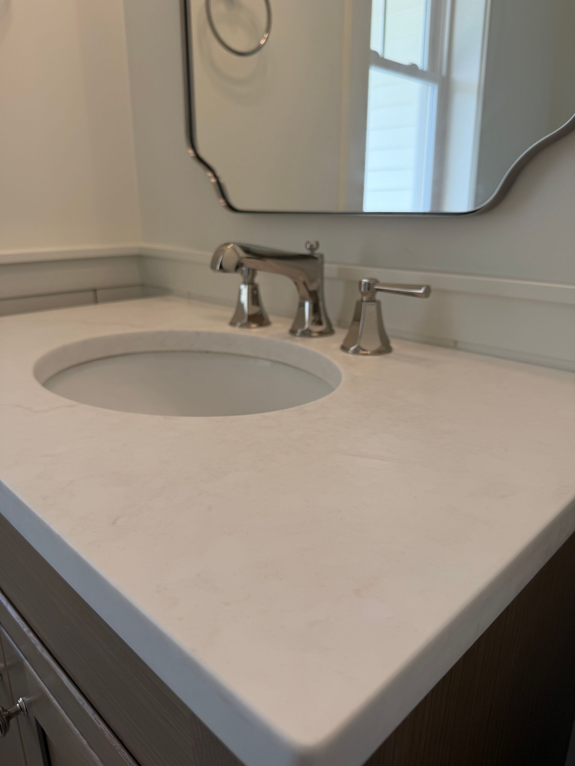 Modern bathroom sink with white countertop, chrome faucet, and wall mirror