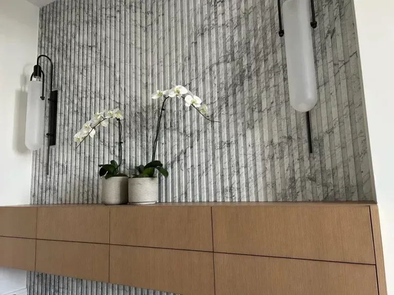 Modern interior with marble wall, wood cabinet, orchid plants, and hanging cylindrical lights