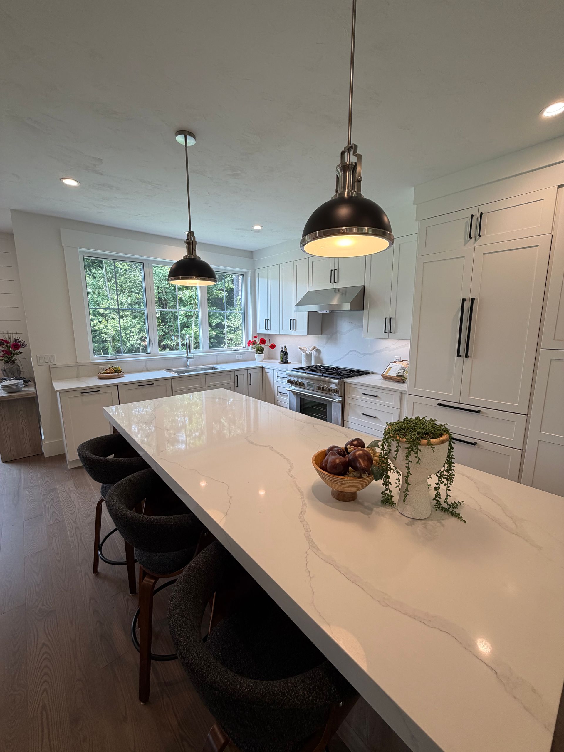 Bright modern kitchen with white island, black pendant lights, and bar stools by a large window