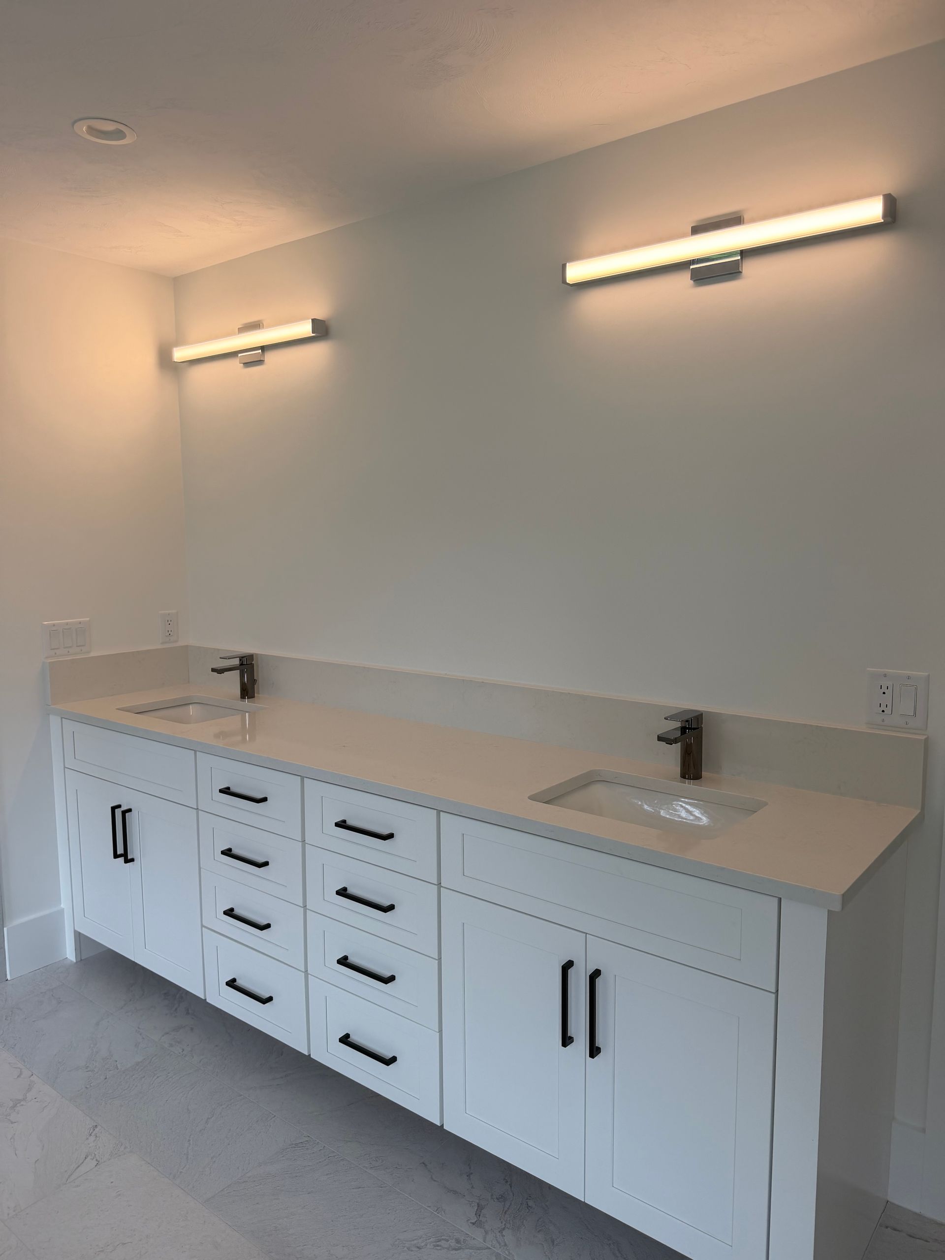 Modern bathroom vanity with double sinks, white cabinets, and wall-mounted lights.