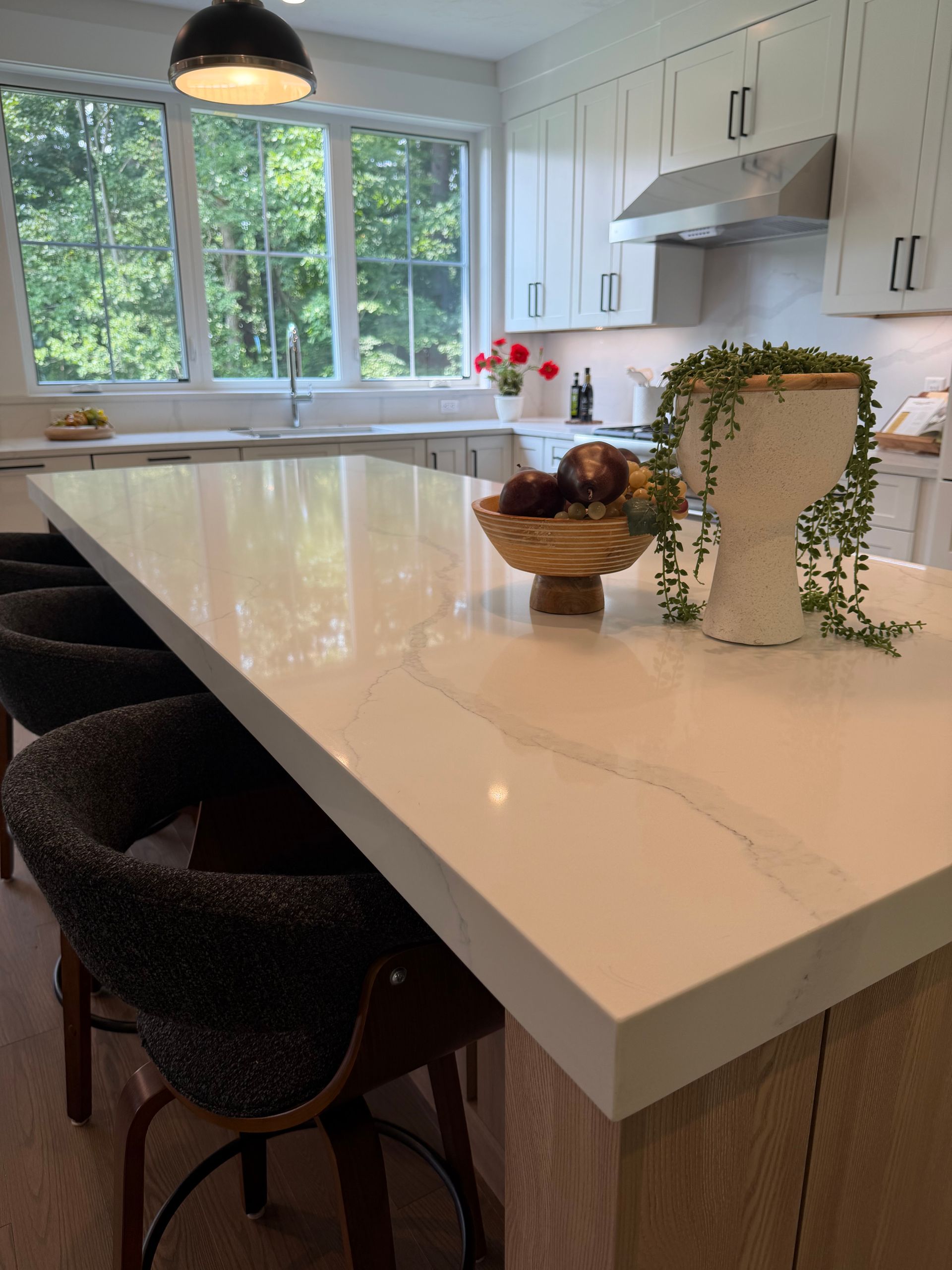 Bright modern kitchen with white island, woven stools, pendant light, and a fruit bowl on the counter