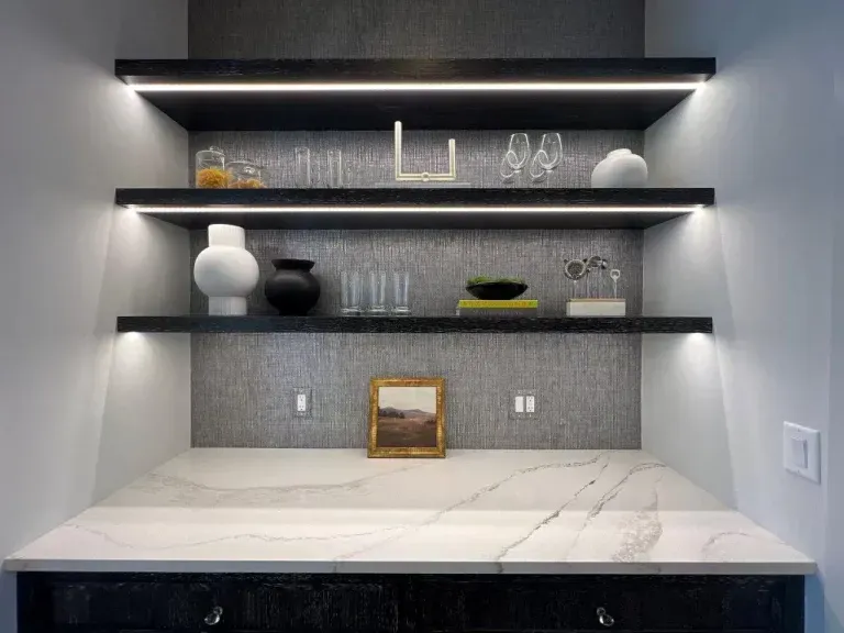 Modern minimalist kitchen nook with lit floating shelves, white veined countertop, and decorative vases