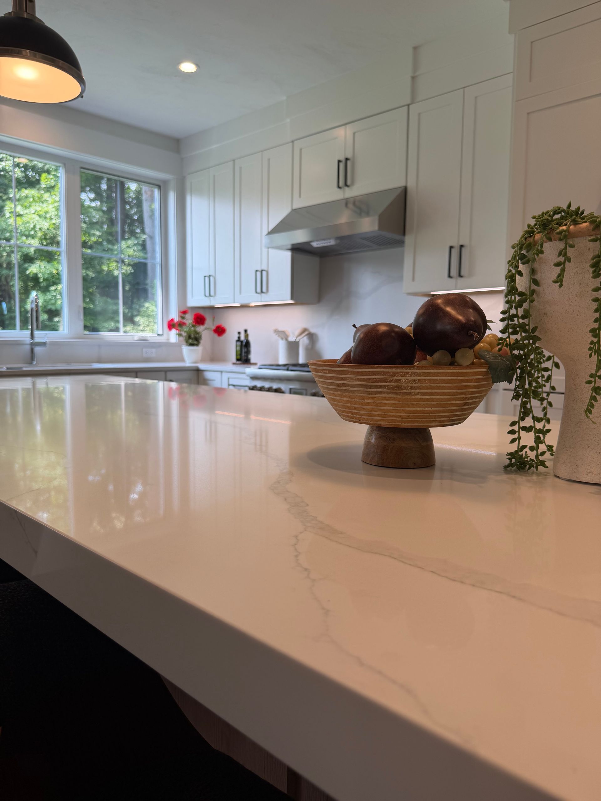 Bright white kitchen with a marble island, basket centerpiece, and window overlooking greenery