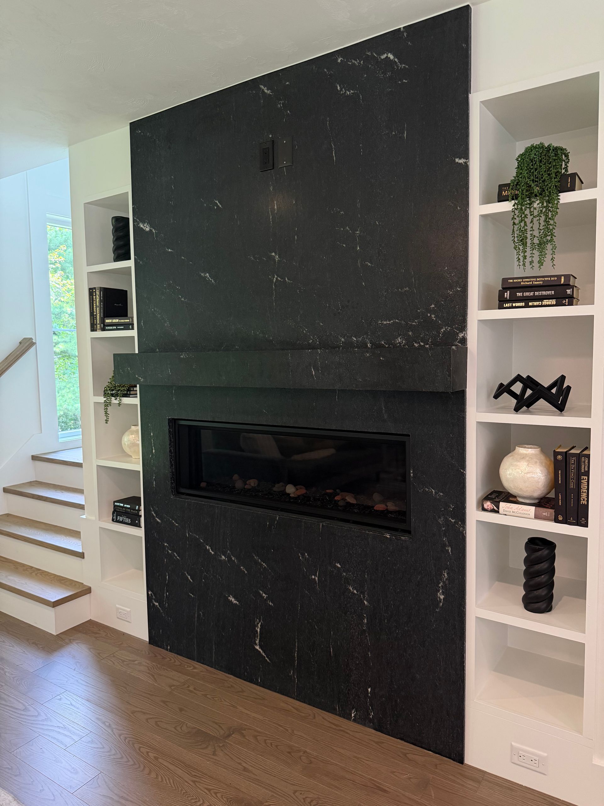 Modern living room fireplace with black tile surround, white built-in shelves, and wood floors