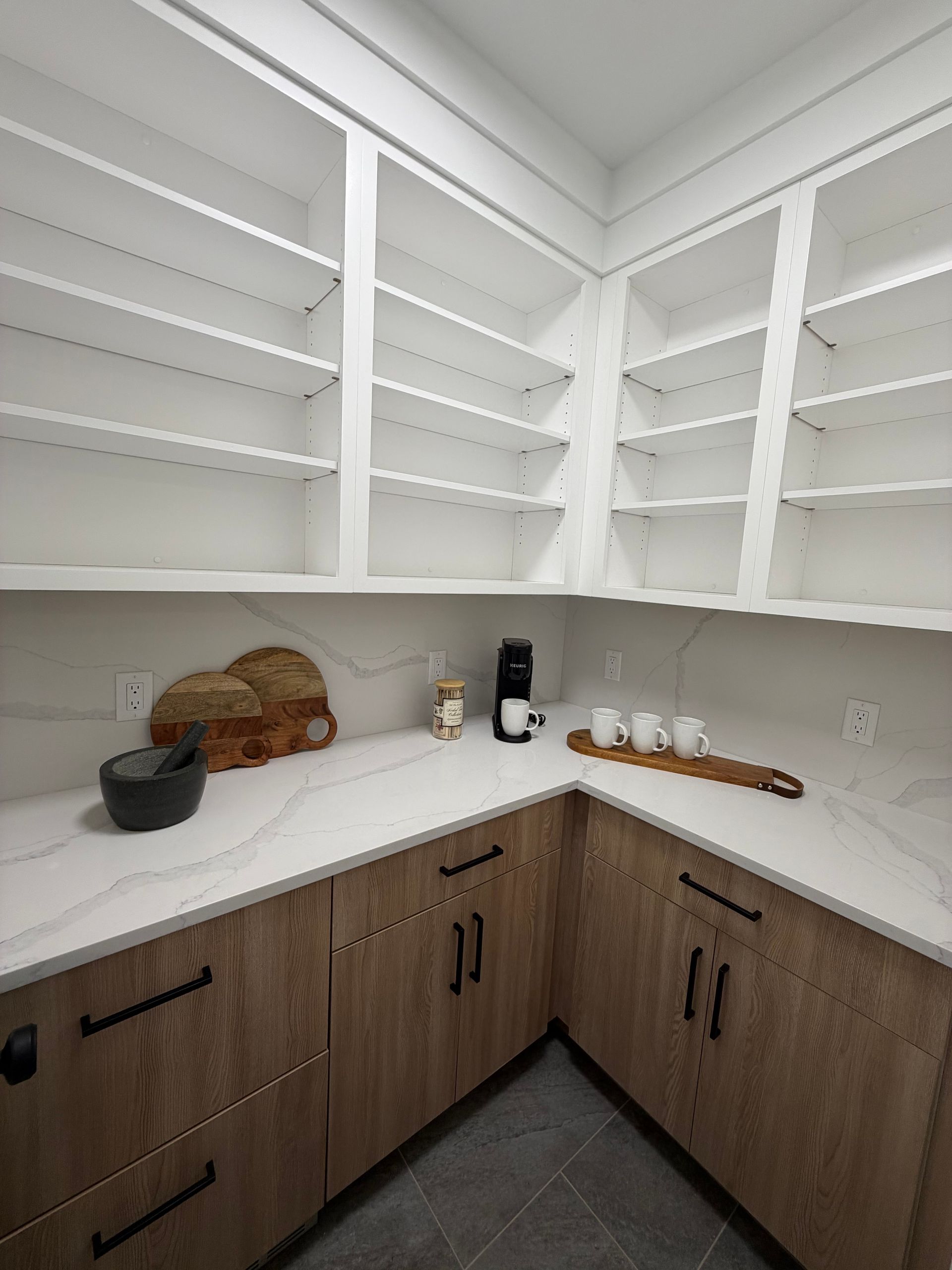 White kitchen pantry with open shelves, wood cabinets, and countertop items including baskets, a bowl, and a coffee maker