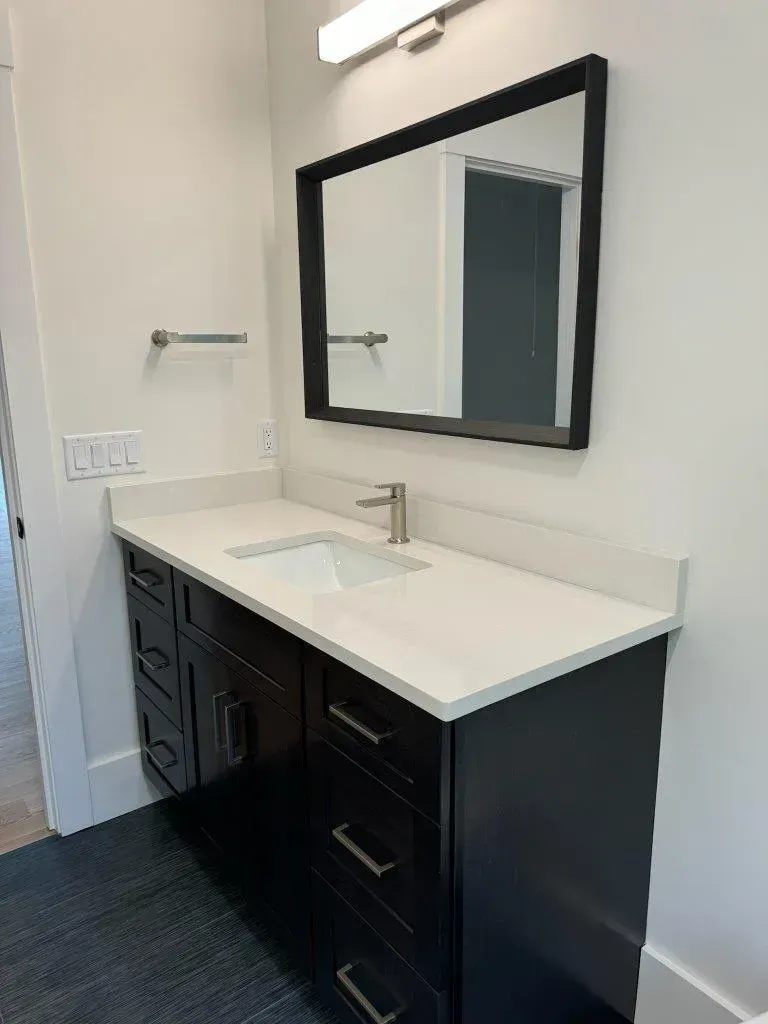 Modern bathroom vanity with black cabinets, white countertop, and large wall mirror