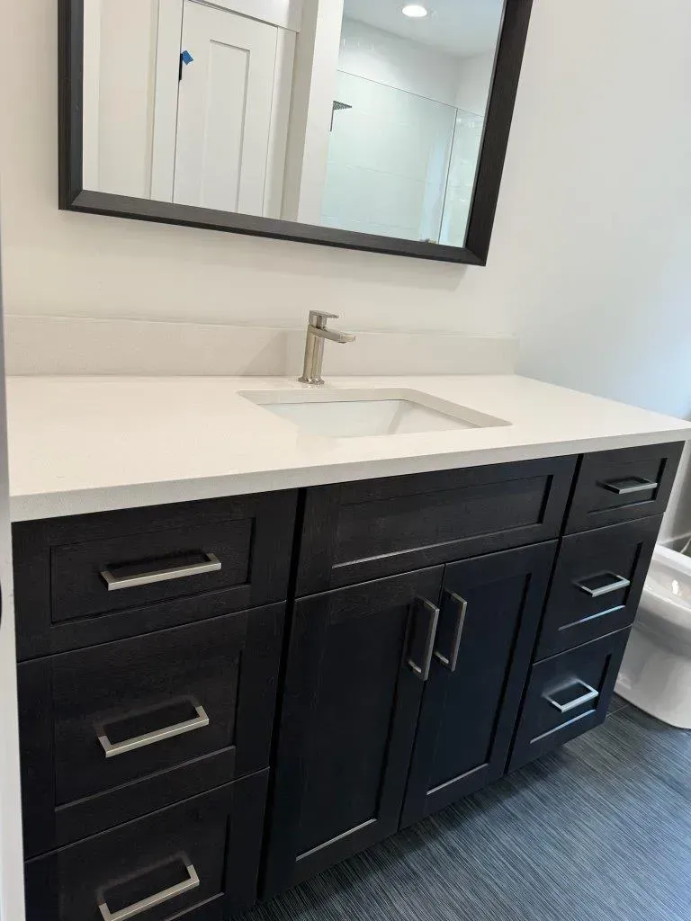 Modern black bathroom vanity with white countertop, sink, and mirror in a bright bathroom.