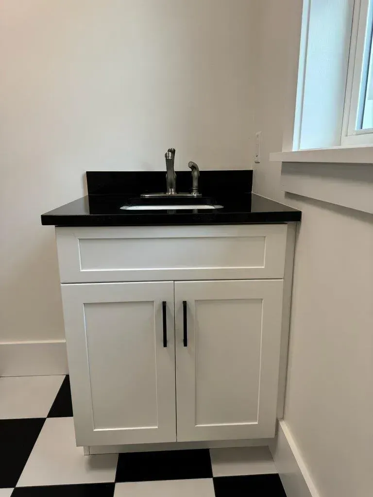 Small white bathroom vanity with black countertop and sink against a tiled floor.